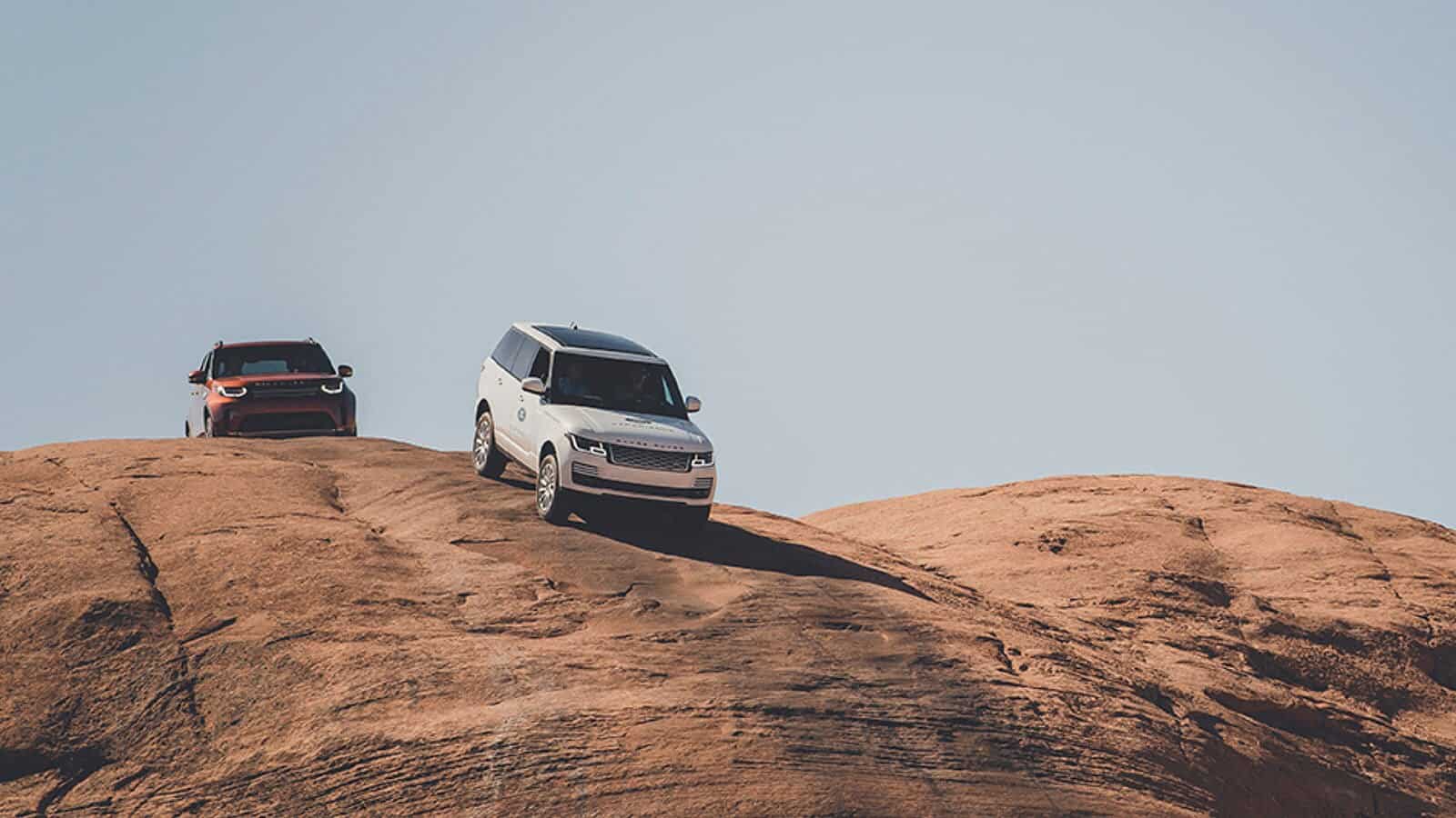 2 Land Rover vehicles driving over the top of a hill
