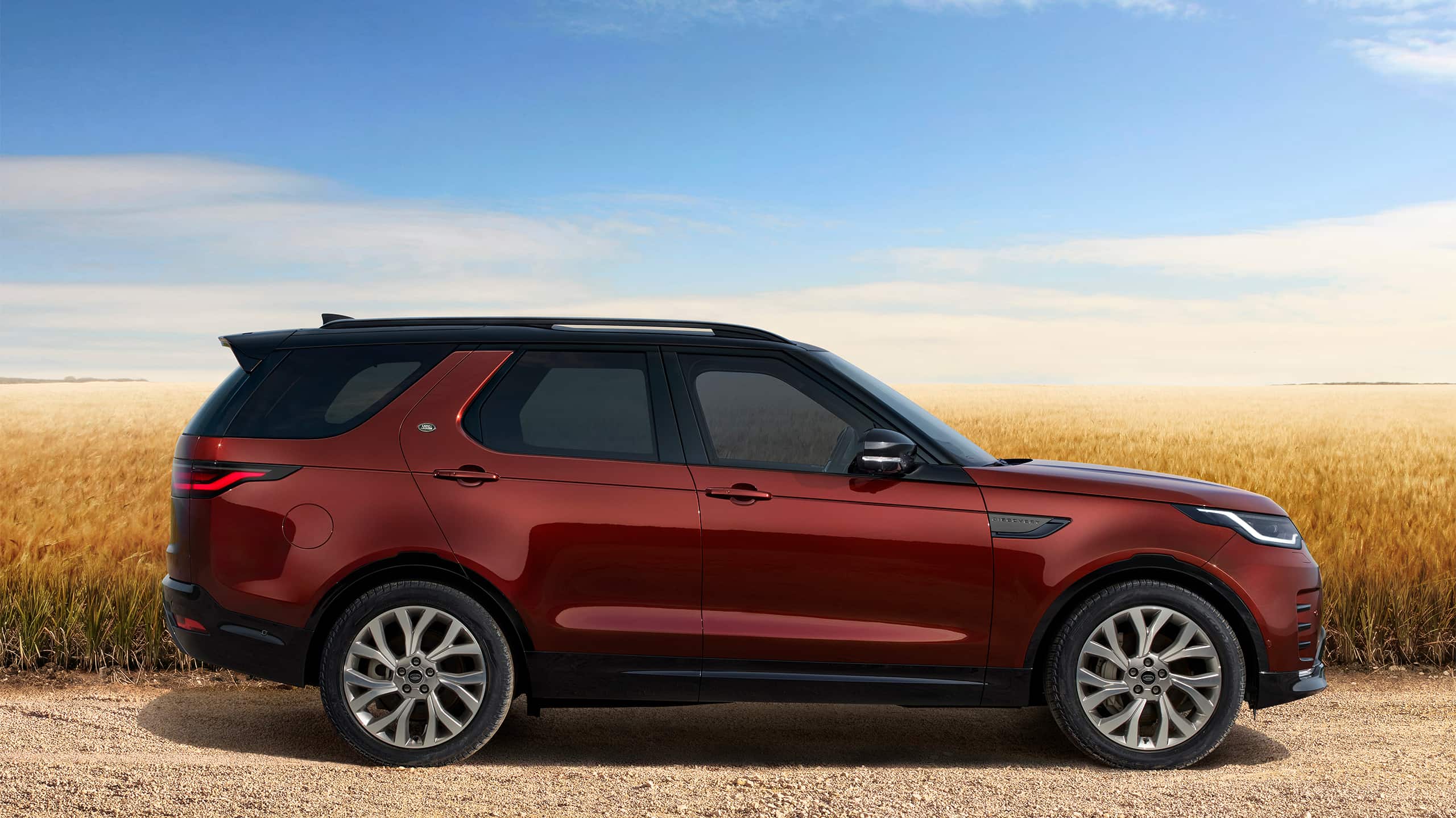 Profile View Of A Red Land Rover Discovery Next To A Field